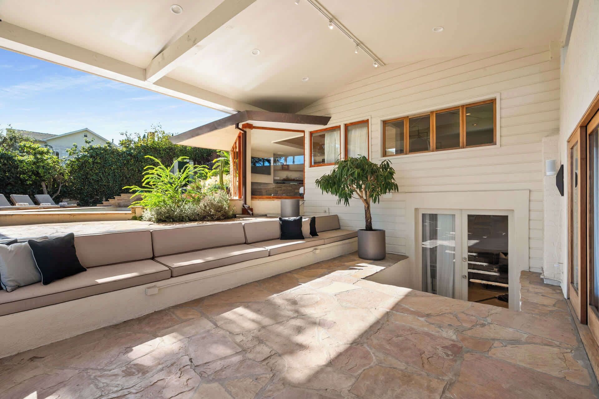 A modern outdoor seating area with stone flooring, a built-in bench, and a potted tree.