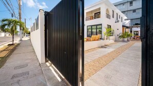 Um condomínio fechado com um edifício branco moderno, um caminho de acesso pavimentado e um pequeno pátio com mobiliário de exterior.