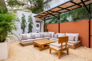 Um espaço ao ar livre moderno com um sofá seccional, uma mesa de centro de madeira e uma pérgola com luzes pendentes.