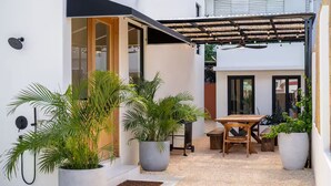 Um pátio moderno ao ar livre com uma mesa e cadeiras de madeira, rodeado por plantas em vasos grandes.