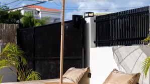 Área de piscina com guarda-sol branco, cadeiras de descanso bege e mesa de madeira.
