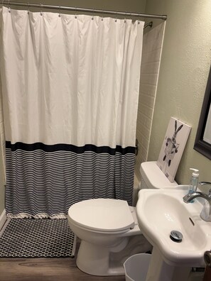 Une salle de bain avec des toilettes blanches, un lavabo blanc, un rideau de douche à rayures et un tapis à motifs.