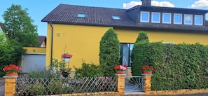 Ett gult hus med ett tak täckt av tegelpannor, ett tydligt synligt nummer ’9’ och en grind vid ingången.