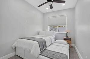Een slaapkamer met een bed, een nachtkastje, een plafondventilator en een raam met zonwering.