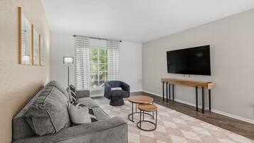 A modern living room with a grey sofa, a black armchair, a TV on a wooden stand, and a patterned rug.