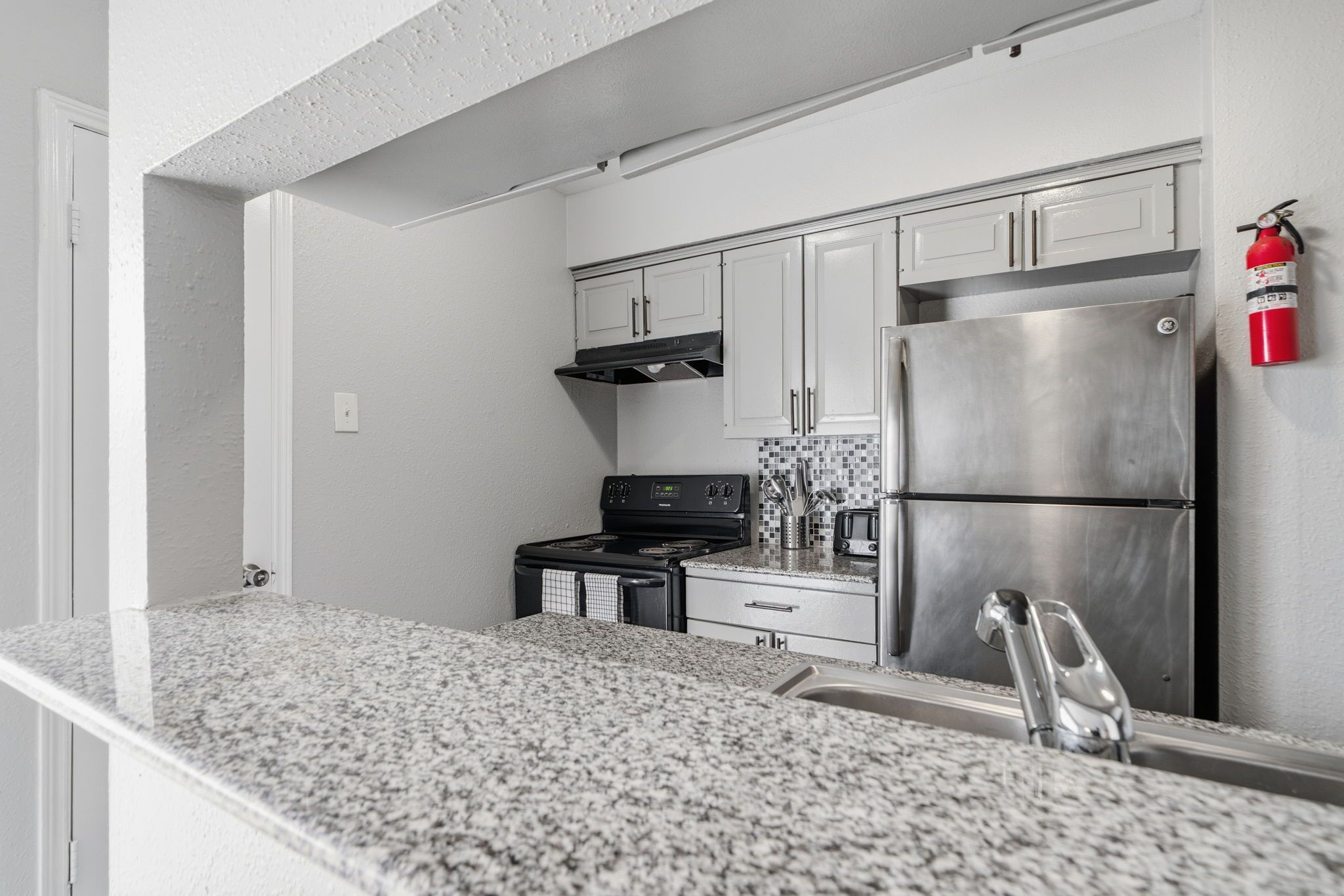 A kitchen with white cabinets, a stainless steel refrigerator, a black stove, and a tiled backsplash.