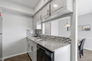 A modern kitchen with white cabinets, a granite countertop, a dishwasher, and a tiled backsplash. - Chic Houston Apt 2BR 2BA (Houston)