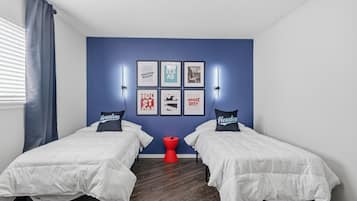 A room with two beds, a red stool, and wall art featuring city names and a cityscape.