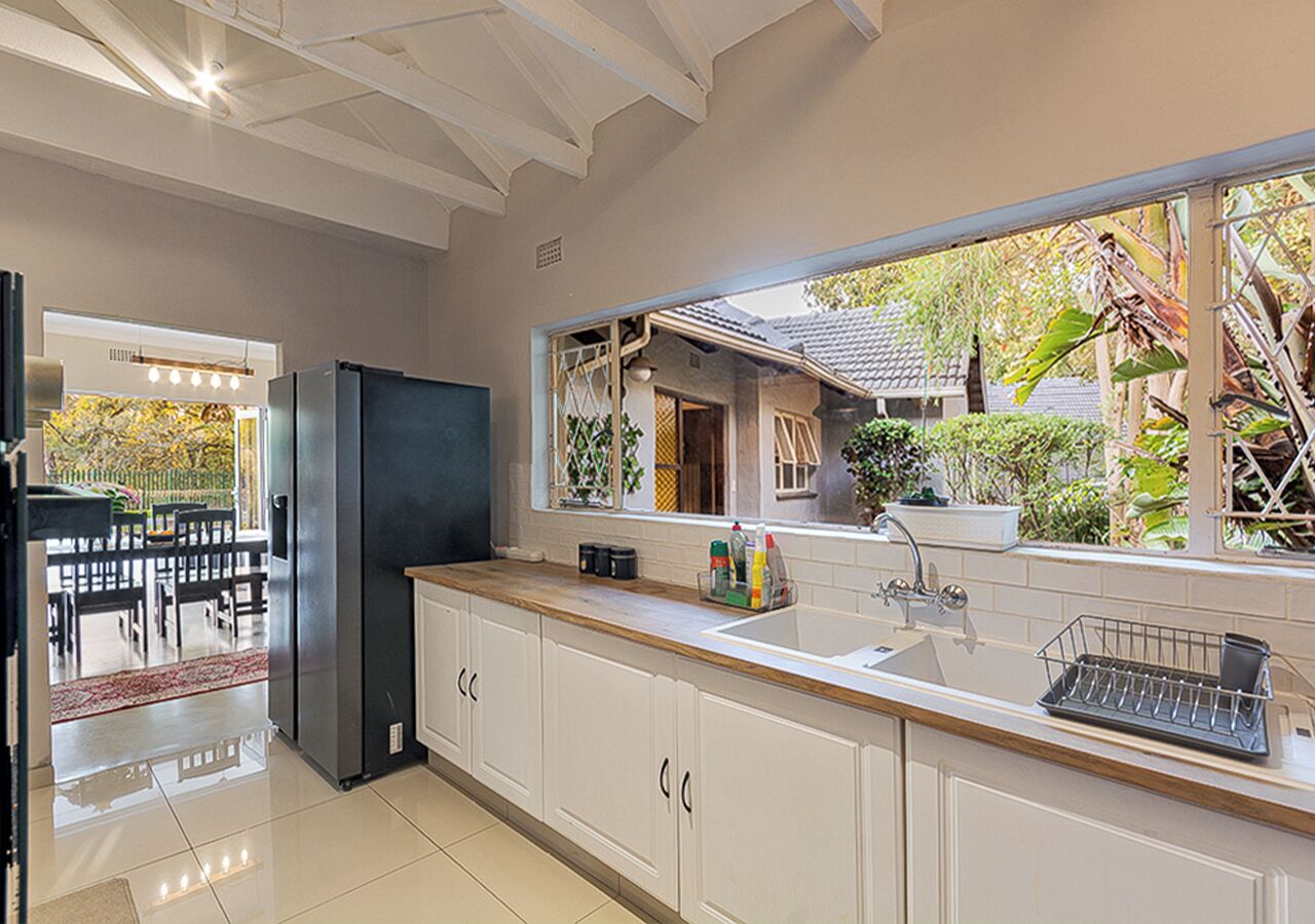 Una cocina moderna con armarios blancos, un refrigerador de acero inoxidable y una ventana con vistas a un jardín.