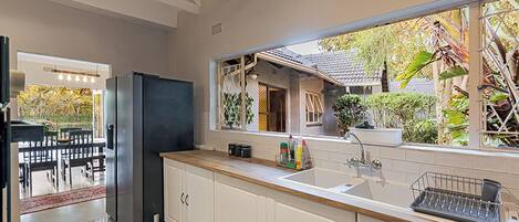 A modern kitchen with white cabinetry, a stainless steel refrigerator, and a window overlooking a garden.