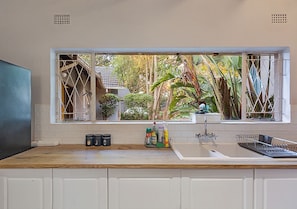 Una cucina con vista dalla finestra, un lavello, pensili e un piano di lavoro con oggetti da cucina.