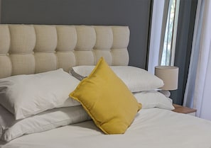 Un letto con testiera trapuntata, biancheria da letto bianca e un cuscino giallo.