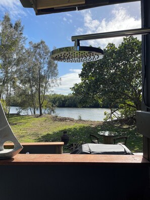 A lakeside view from a window with a table and chairs, a hanging light fixture, and trees surrounding the area. - River frontage on Maroochy River, Sunshine Coast! (Maroochy River)