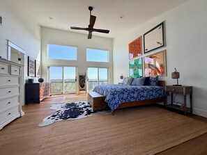Ein geräumiges Schlafzimmer mit einem großen Bett, einem Deckenventilator und Blick durch die großen Fenster.
