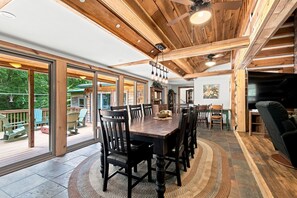 A spacious dining area with a large wooden table and chairs, a ceiling fan, and a view through large glass doors to an outdoor deck.