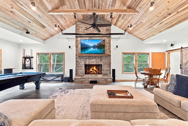A spacious living room with a stone fireplace, a pool table, and a cozy seating area.