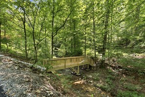 A wooden bridge in a forested area with a rocky path on one side and dense green foliage on the other.