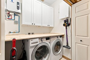 A laundry room with two front-loading washing machines, a red vacuum cleaner, and a water heater on the wall. - 8-bedroom nature resort w/ pool just 30 minutes from Nashville! (Hendersonville)