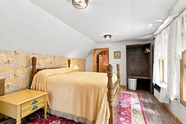 A bedroom with a bed, a bedside table, a wooden wardrobe, a window with curtains, and a patterned carpet.