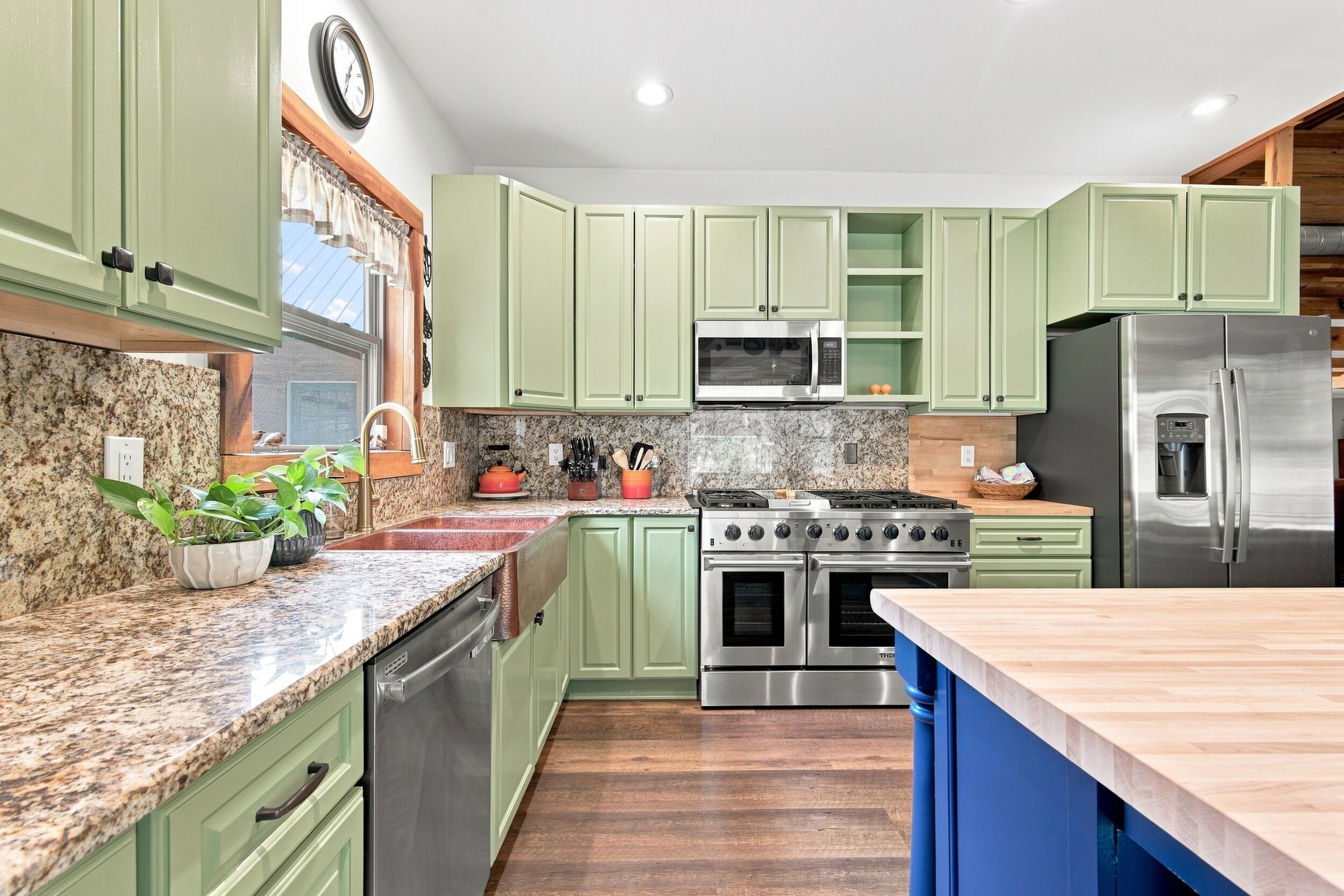 Une cuisine avec des meubles de couleur verte, un réfrigérateur en acier inoxydable, un four à micro-ondes, une cuisinière et un lave-vaisselle.