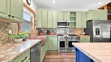 Une cuisine avec des meubles de couleur verte, un réfrigérateur en acier inoxydable, un four à micro-ondes, une cuisinière et un lave-vaisselle.