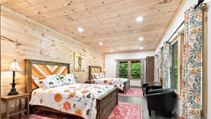 A wooden cabin bedroom with two beds, a desk, and a chair.