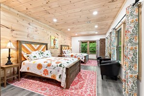A wooden cabin bedroom with two beds, a desk, and a chair.