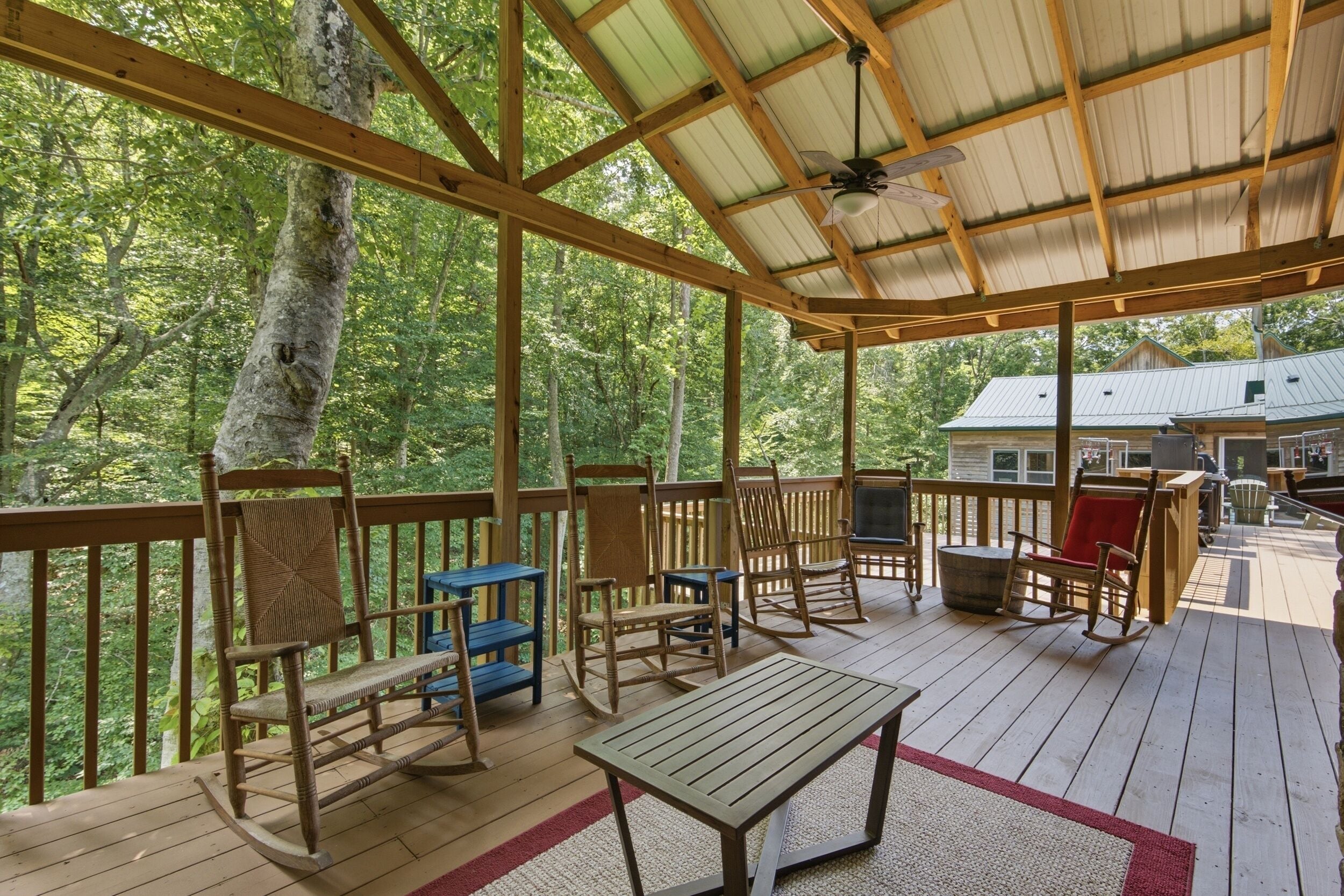 Une terrasse couverte, dotée de mobilier en bois, d’où l’on peut apercevoir une maison au loin.