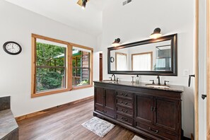A bathroom with a wooden vanity, a large mirror, and a window with a view of greenery.