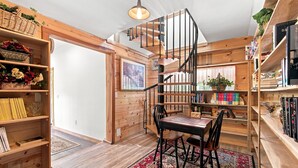 A wooden interior with a spiral staircase, bookshelves, and a chess table.