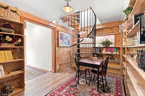 A wooden interior with a spiral staircase, bookshelves, and a chess table.