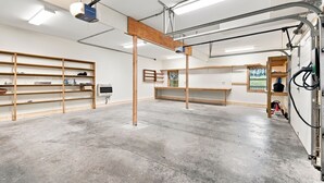 A spacious room with concrete flooring, wooden shelving units, a central wooden beam structure, and a window with a view.