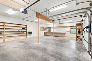 A spacious room with concrete flooring, wooden shelving units, a central wooden beam structure, and a window with a view.