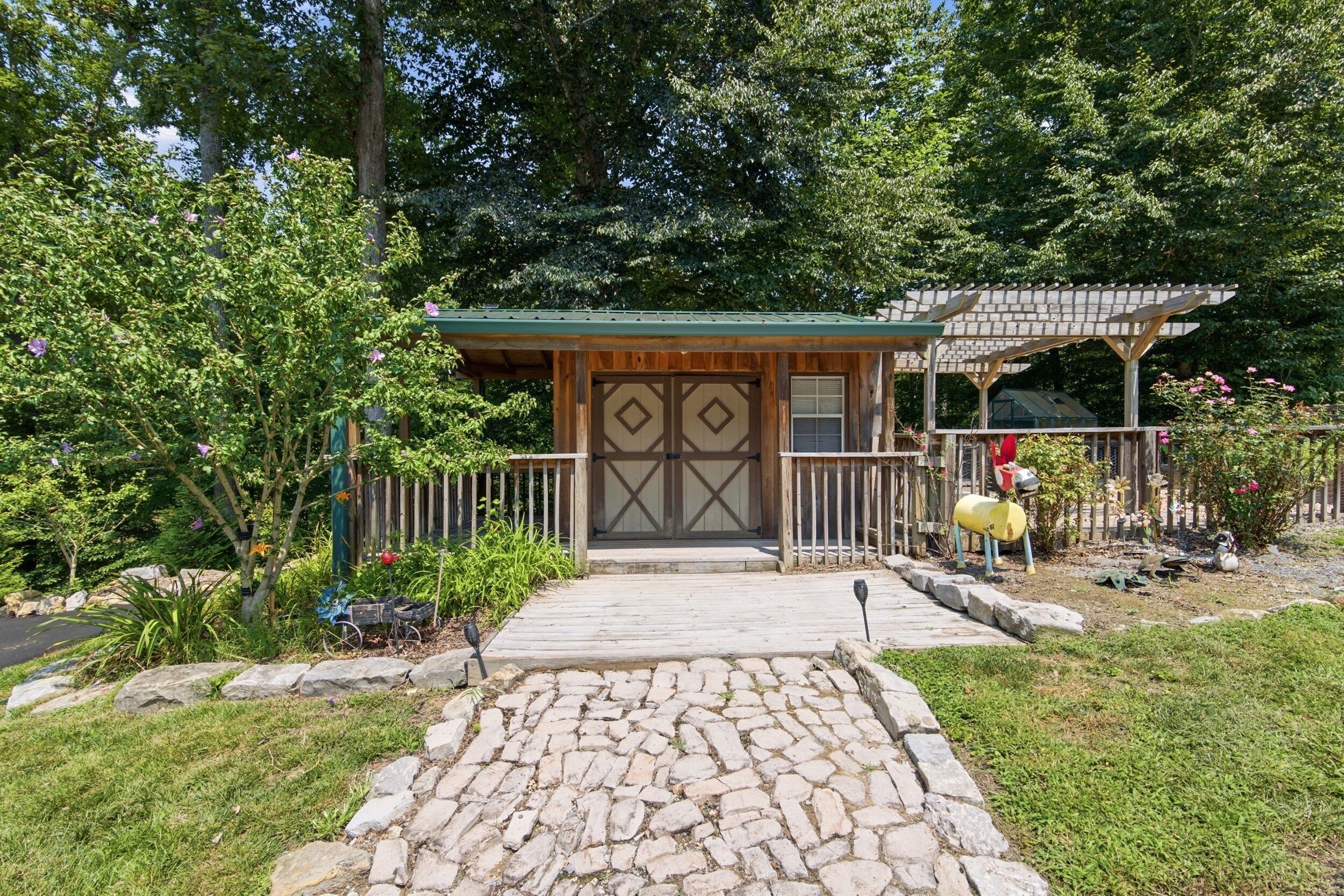 Un bâtiment rustique en bois, doté d’un toit végétalisé, d’un chemin de pierre menant à l’entrée et d’un jardin clos où poussent diverses plantes et fleurs.