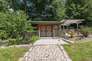 A rustic wooden building with a green roof, a stone pathway leading to the entrance, and a fenced garden area with various plants and flowers. - 8-bedroom nature resort w/ pool just 30 minutes from Nashville! (Hendersonville)