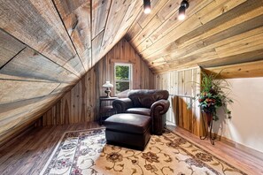 A cozy attic room with wooden walls, a leather sofa, a small table, and a decorative plant.