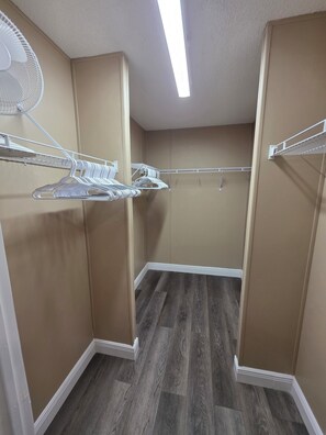 A walk-in closet with wooden flooring, beige walls, and white shelving units. - 1800 sq ft, 3-bed, 2- bath, 2 plus acres in Gulf Hammock Florida. (Morriston)