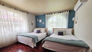 A room with two beds, wooden flooring, and a window with curtains.