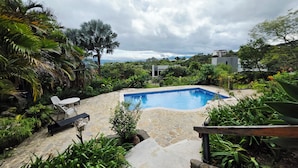 A swimming pool surrounded by lush greenery, stone pathways, and outdoor furniture.