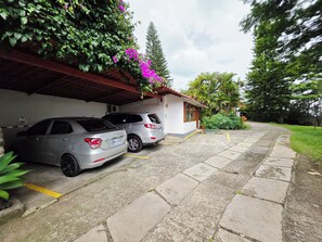 A parking area with two cars parked under a covered structure, adjacent to a building with a red roof.