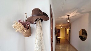 A hallway with a wall-mounted hat and macramé decoration, a wooden door, and a dining area in the background.
