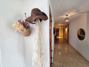 A hallway with a wall-mounted hat and macramé decoration, a wooden door, and a dining area in the background.