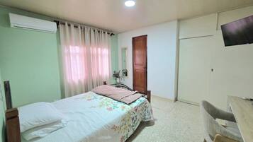 Une chambre à coucher comprenant un lit, un bureau, une chaise, un appareil de climatisation, une porte et un téléviseur.