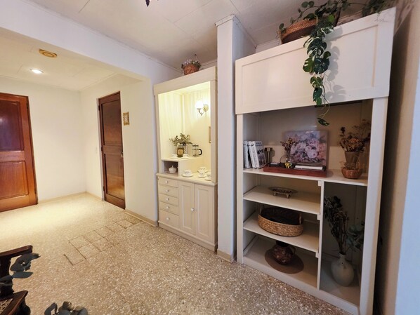 Un pasillo con una puerta de madera, un armario blanco con cajones y un estante con adornos.