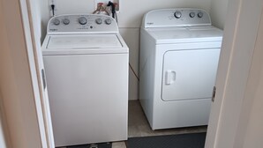 A laundry room with two white Whirlpool washers and dryers, a black doormat with 'WELCOME' and a deer design, and a black mat on the floor. - 3-bedroom house in peaceful Stacyville  short distance to mt katahdin (Stacyville)