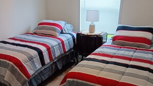 A bedroom with two beds, each with striped bedding, a bedside table with a lamp, and a window with blinds. - 3-bedroom house in peaceful Stacyville  short distance to mt katahdin (Stacyville)