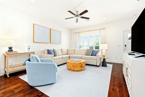 Ein modernes Wohnzimmer mit einem Ecksofa, einem runden Couchtisch, einem Fernseher und einem Deckenventilator.