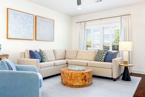 Ein Wohnzimmer mit einem beigefarbenen Ecksofa, einem runden Holztisch und einem Beistelltisch mit einer Lampe.