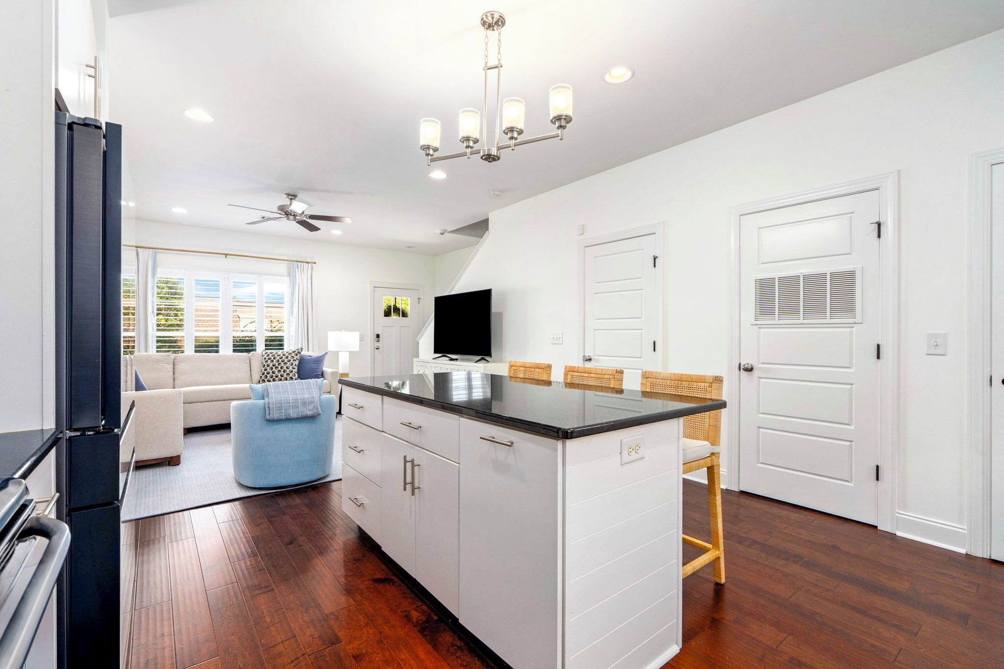 A modern kitchen with a central island, a dining area with a table and chairs, a sofa, and a ceiling fan.