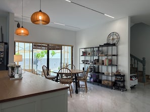 A modern kitchen with a wooden countertop, two pendant lights, a dining area with chairs, a bookshelf, and a staircase. - Villa with Office, Gym, Jacuzzi & Dryer near CIQ (Johor Bahru)